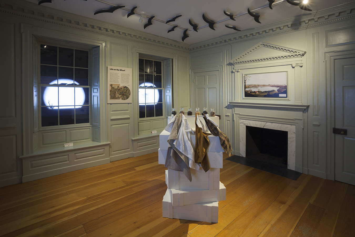 Photograph of an austere period room with green painted wood paneling, shadow puppets in the windows, and an interactive touch/smell station in the center of the room.